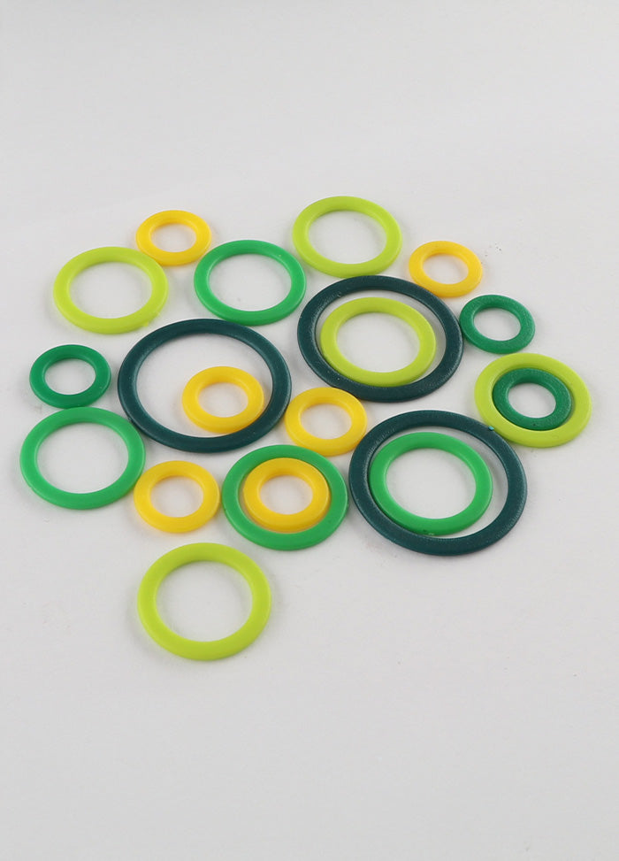 Colourful rubber O-rings in yellow and green on a white surface, used as practical stitch markers for knitting projects.