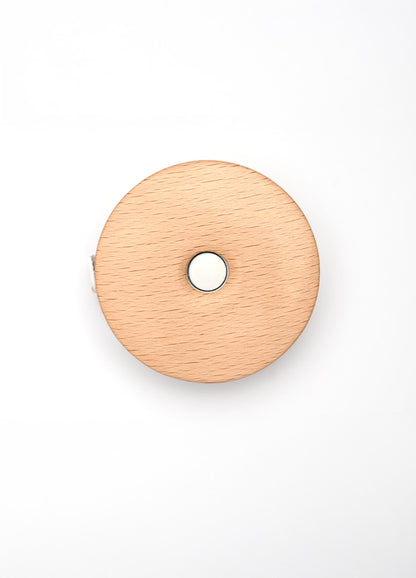 Teal wooden tape measure with a lotus design, featuring a central hole for smooth retraction of the 152cm/60” tape.