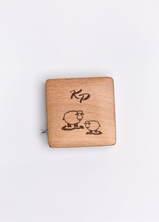 A beechwood box with a sheep motif and KP logo, housing a 150cm tape measure with metric and imperial markings.