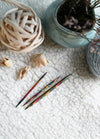 Three knitting needles and colourful yarn arranged on a white rug, showcasing their grooves and tapered tips for easy use.