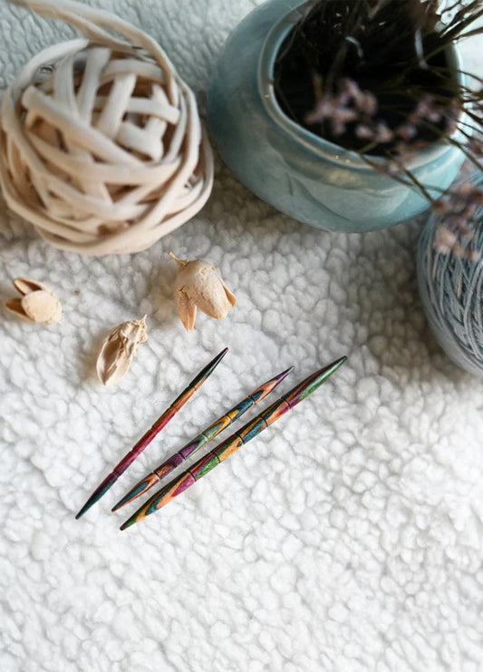 Three knitting needles and colourful yarn arranged on a white rug, showcasing their grooves and tapered tips for easy use.