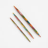  Three colorful Symfonie wood knitting needles on a white surface, featuring grooves and tapered tips for easy knitting.