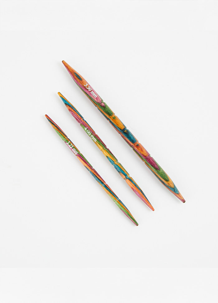  Three colorful Symfonie wood knitting needles on a white surface, featuring grooves and tapered tips for easy knitting.
