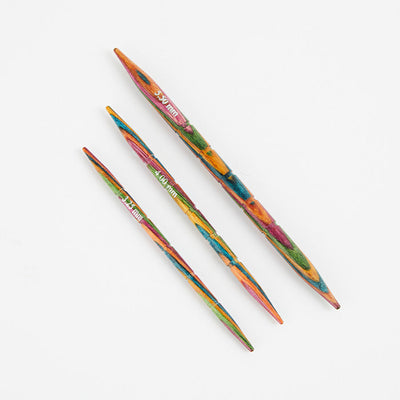  Three colorful Symfonie wood knitting needles on a white surface, featuring grooves and tapered tips for easy knitting.