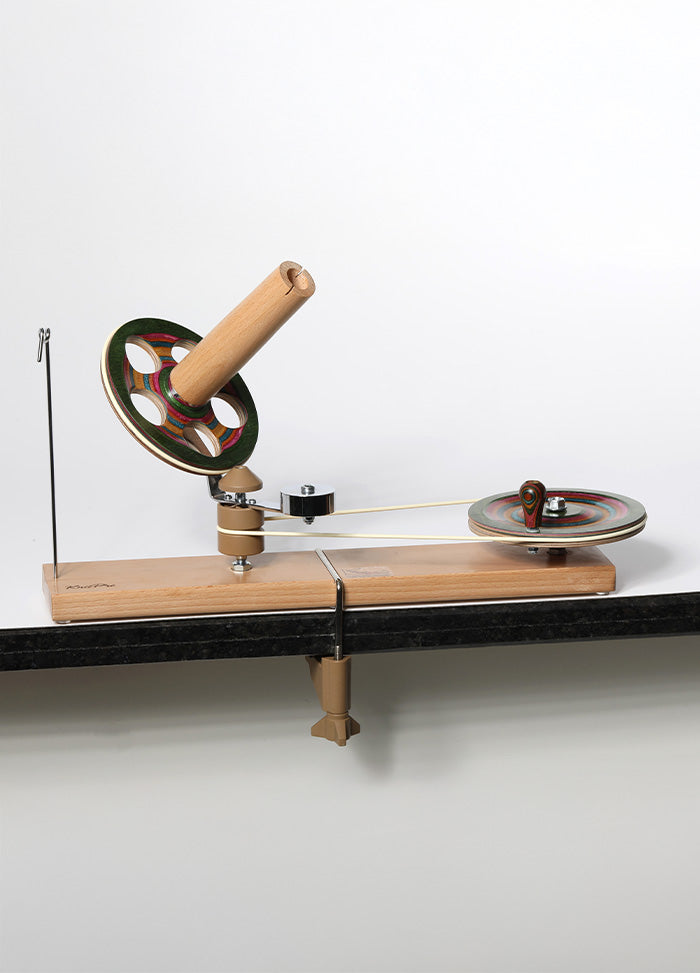 A handcrafted spinning wheel on a wooden stand, made of colorful laminated birch, designed for smooth yarn winding.