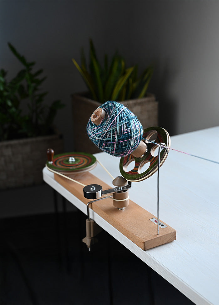 A handcrafted spinning wheel on a table, with a colorful ball of yarn, designed for smooth and efficient yarn winding.