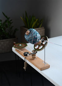 A handcrafted spinning wheel on a table, with a colorful ball of yarn, designed for smooth and efficient yarn winding.