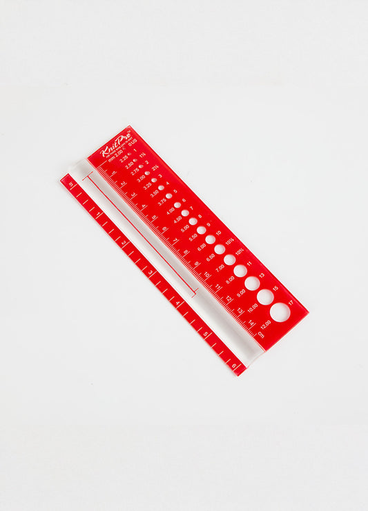 A red ruler against a white background, designed to measure knitting needle sizes and gauge with a clear magnifying feature.