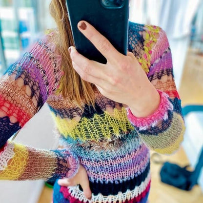 Mirror selfie of a person wearing a vibrant, multicolored knitted sweater featuring eclectic patterns in pink, purple, blue, yellow, and green. The person’s face is partially hidden by the phone, highlighting the bold and expressive knitwear design.