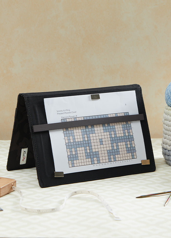  A crafting table features a magma chart keeper, a cross stitch kit, and a book, highlighting essential tools for crafters.