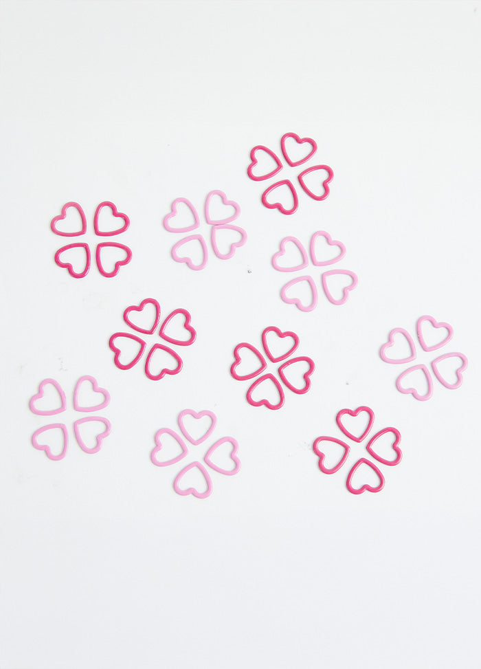 A pile of pink heart-shaped metal stitch markers on a white surface.