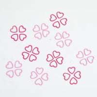 A pile of pink heart-shaped metal stitch markers on a white surface.