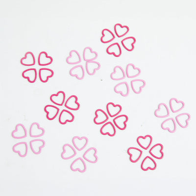 A pile of pink heart-shaped metal stitch markers on a white surface.