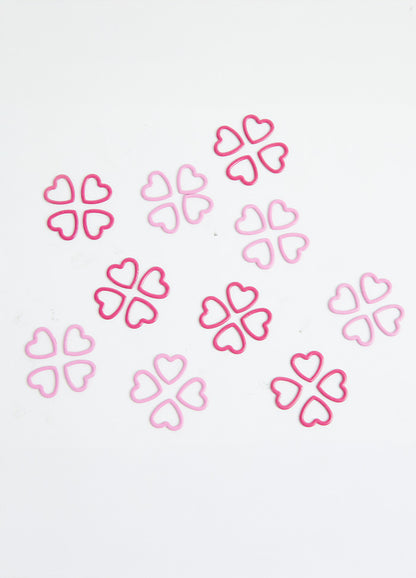 A pile of pink heart-shaped metal stitch markers on a white surface.
