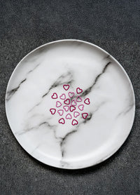 A white plate featuring a pink heart stitch markers, designed for the Magnetic Knitter's Necklace Kit.