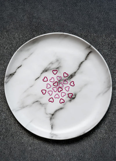 A white plate featuring a pink heart stitch markers, designed for the Magnetic Knitter's Necklace Kit.