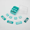 A set of blue and teal rectangular knitting blockers  with metal prongs, some inside a clear plastic box and others arranged outside on a white surface.
