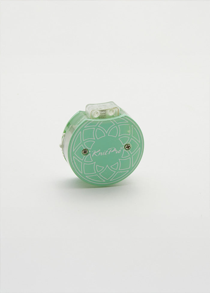 Row counter with a flower design in green and white, used for tracking rows on a teal knitting tool in a cotton pouch