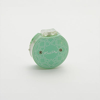 Row counter with a flower design in green and white, used for tracking rows on a teal knitting tool in a cotton pouch