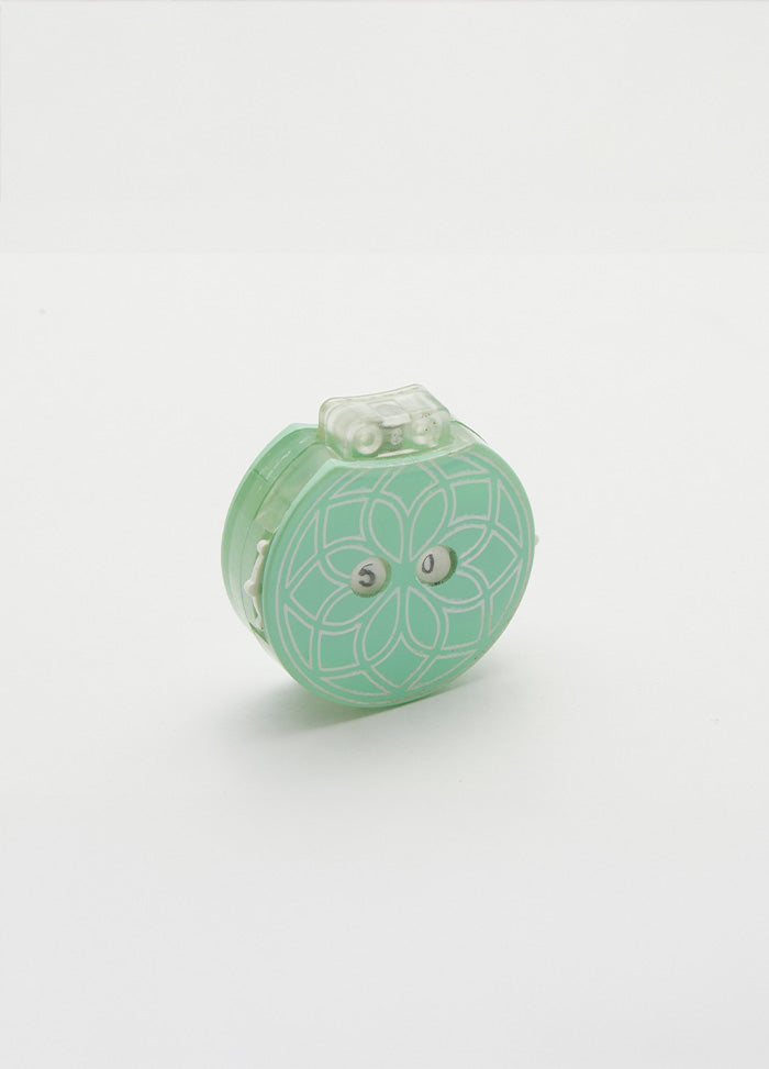Small green row counter with a flower design, part of a teal knitting tool for tracking rows, in a drawstring cotton case.
