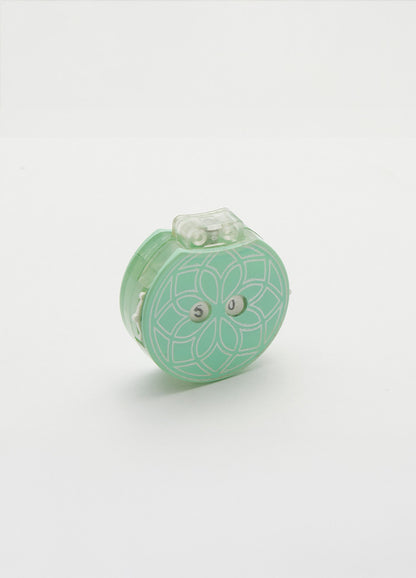 Small green row counter with a flower design, part of a teal knitting tool for tracking rows, in a drawstring cotton case.