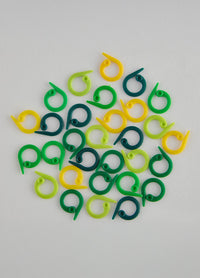 A pile of bold green and yellow plastic stitch markers for knitting and crochet, designed for easy visibility and use.