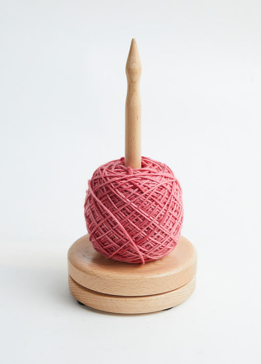  A yarn ball positioned on a beech wood dispenser, designed to maintain tension and prevent tangles while knitting.