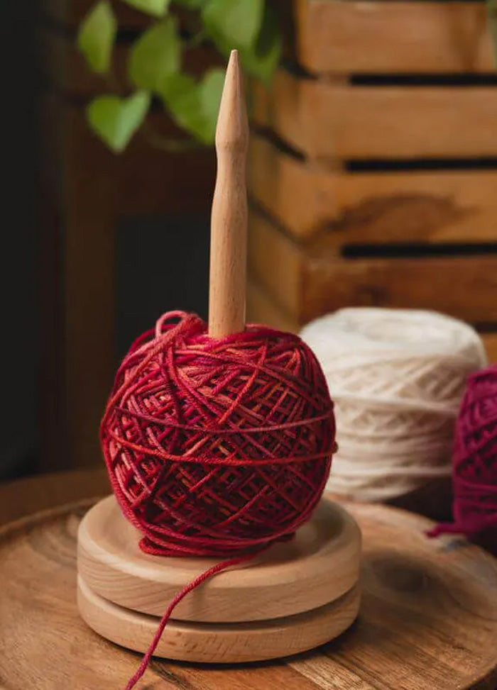 A ball of yarn resting on a natural beech wood stand, designed to maintain tension and prevent slipping during knitting.