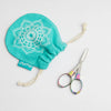 A pair of colorful, foldable scissors with a shiny finish next to a bag adorned with a floral design.