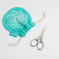 A pair of colorful, foldable scissors with a shiny finish next to a bag adorned with a floral design.