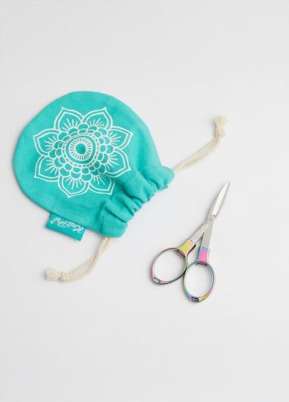 A pair of colorful, foldable scissors with a shiny finish next to a bag adorned with a floral design.