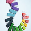 A circular arrangement of colorful plastic blockers with pins, designed for knitting, crochet, and weaving projects.