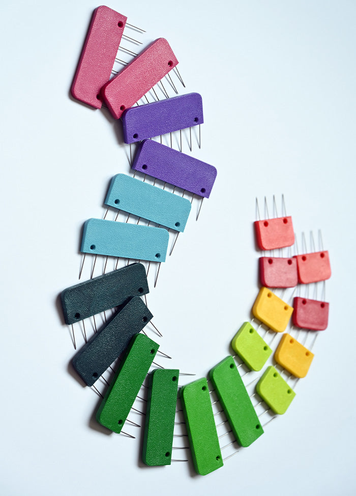A circular arrangement of colorful plastic blockers with pins, designed for knitting, crochet, and weaving projects.