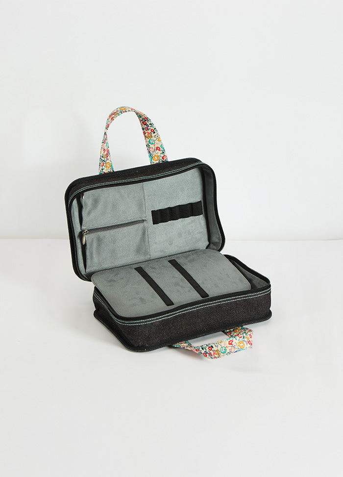 Black and white knitting case with zipper, featuring floral trim, designed for carrying yarn and project accessories.