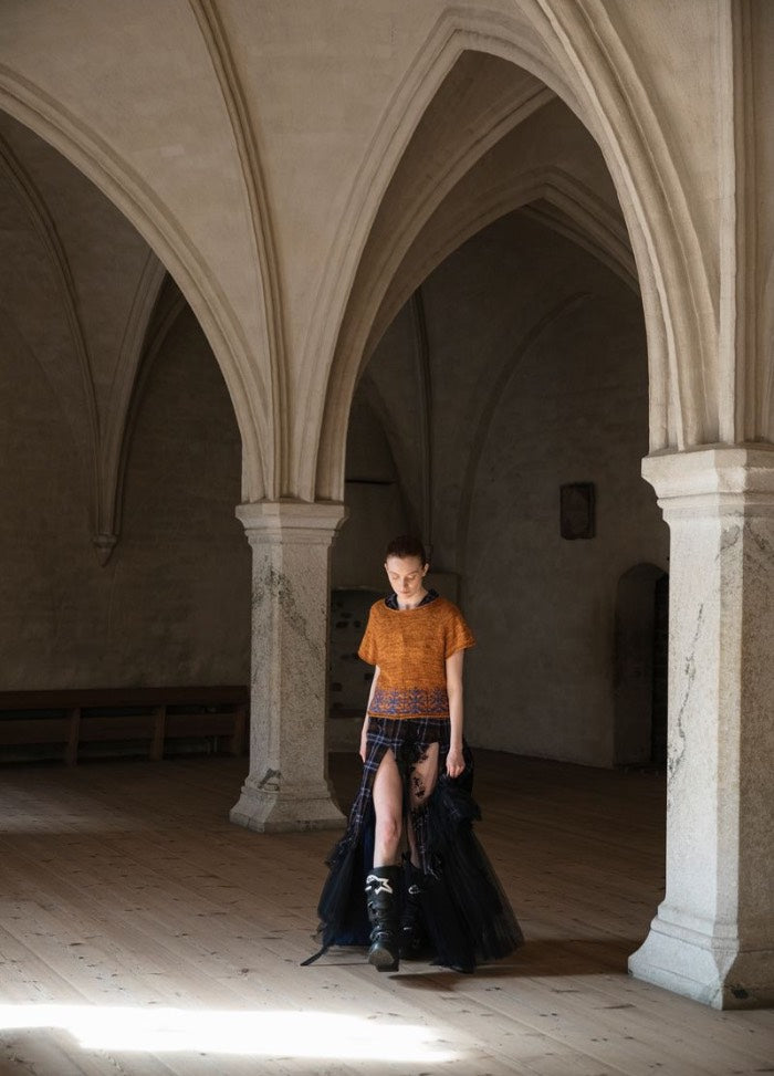 Lahde Kukka Kulkemahan: orange top paired with a black patterned skirt, photographed in a grand arched stone interior.