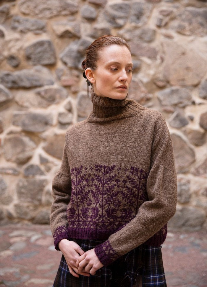 Metsan Vaki: brown turtleneck sweater with purple motifs on the lower torso and sleeves, photographed against a stone wall.