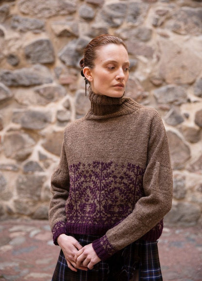 Metsan Vaki: brown turtleneck sweater with purple motifs on the lower torso and sleeves, photographed against a stone wall.