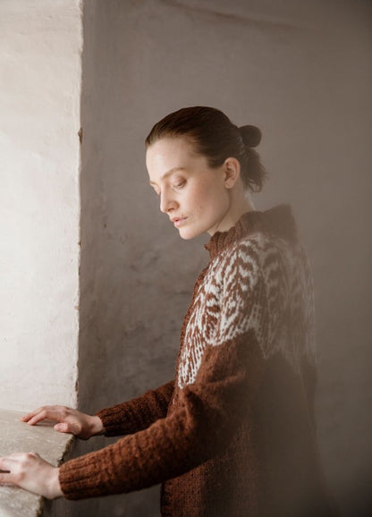 Raudan Synty: brown cardigan with white patterned yoke, photographed against a light-colored wall.