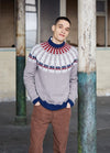 Young man in a festive sweater leans casually against a weathered pillar in an industrial setting. He smiles softly, conveying a relaxed, cheerful mood.