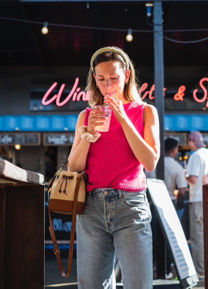 Send Me a Postcard Top: Pink sleeveless knit styled with jeans and a beige handbag, set in a lively outdoor scene.