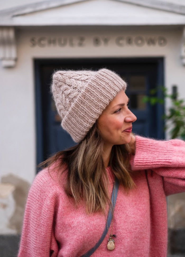 Twist It Beanie: Cozy knit hat styled with a pink sweater, photographed in front of a building entrance.
