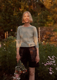 Lucienne Sweater: light-colored knit sweater worn with dark shorts, photographed in a garden setting with flowers and greenery.
