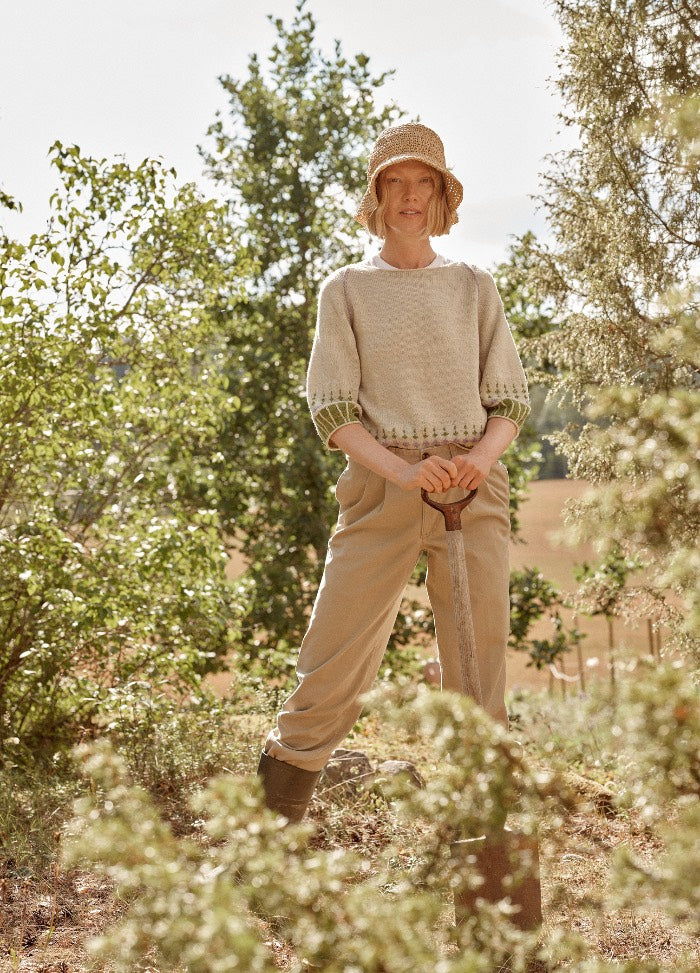 Facette Sweater: light-colored knit sweater with intricate patterns and three-quarter sleeves, worn outdoors with beige pants and boots.