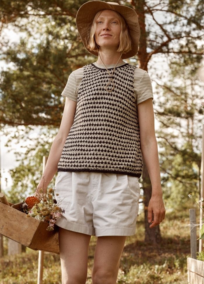 Fossora Top: black and white patterned sleeveless knit top worn with white shorts, photographed outdoors with a flower-filled wooden box.