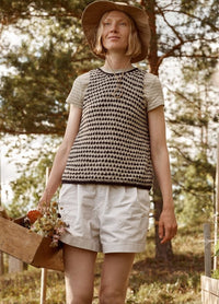 Fossora Top: black and white patterned sleeveless knit top worn with white shorts, photographed outdoors with a flower-filled wooden box.