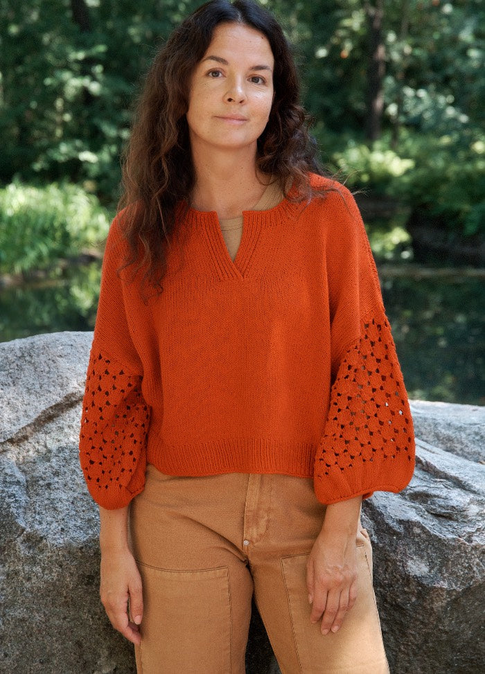 Flecks of Sunshine Top: model in orange lace-sleeved knit top with V-neck, standing outdoors near rocks and greenery.