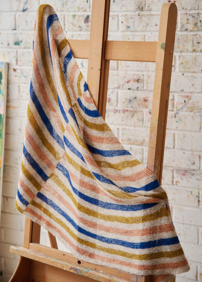 Modernist Shawl: striped knit shawl in blue, mustard, peach, and white, draped over a wooden easel.