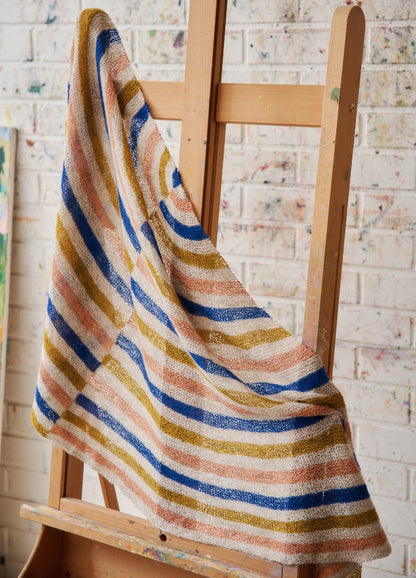 Modernist Shawl: striped knit shawl in blue, mustard, peach, and white, draped over a wooden easel.