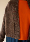 Brown hand-knitted cardigan with textured front edges, worn over an orange shirt.