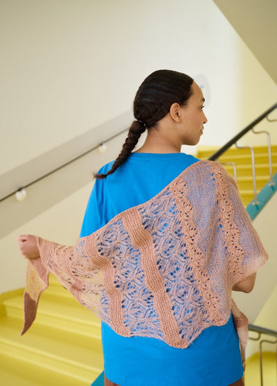 Lace-patterned shawl in peach and light purple, draped over a blue shirt, with yellow stairs and teal railings in the background.